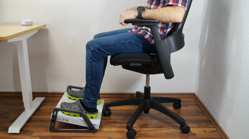 Person auf einem Bürostuhl mit Fußstütze am Schreibtisch