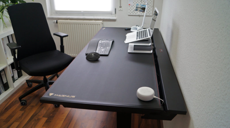 Seitlicher Blick auf Schreibtisch mit Laptop auf Laptopständer, separater Tastatur und Maus