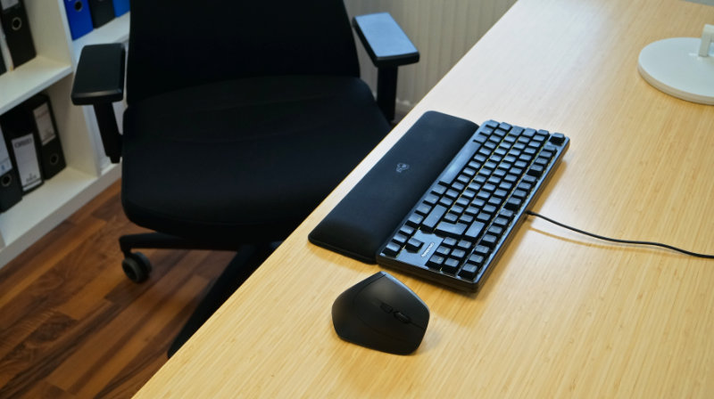 CHERRY MW 4500 im Test – Ergonomische, vertikale Maus steht neben Tastatur auf einem Schreibtisch, hinten ein Bürostuhl