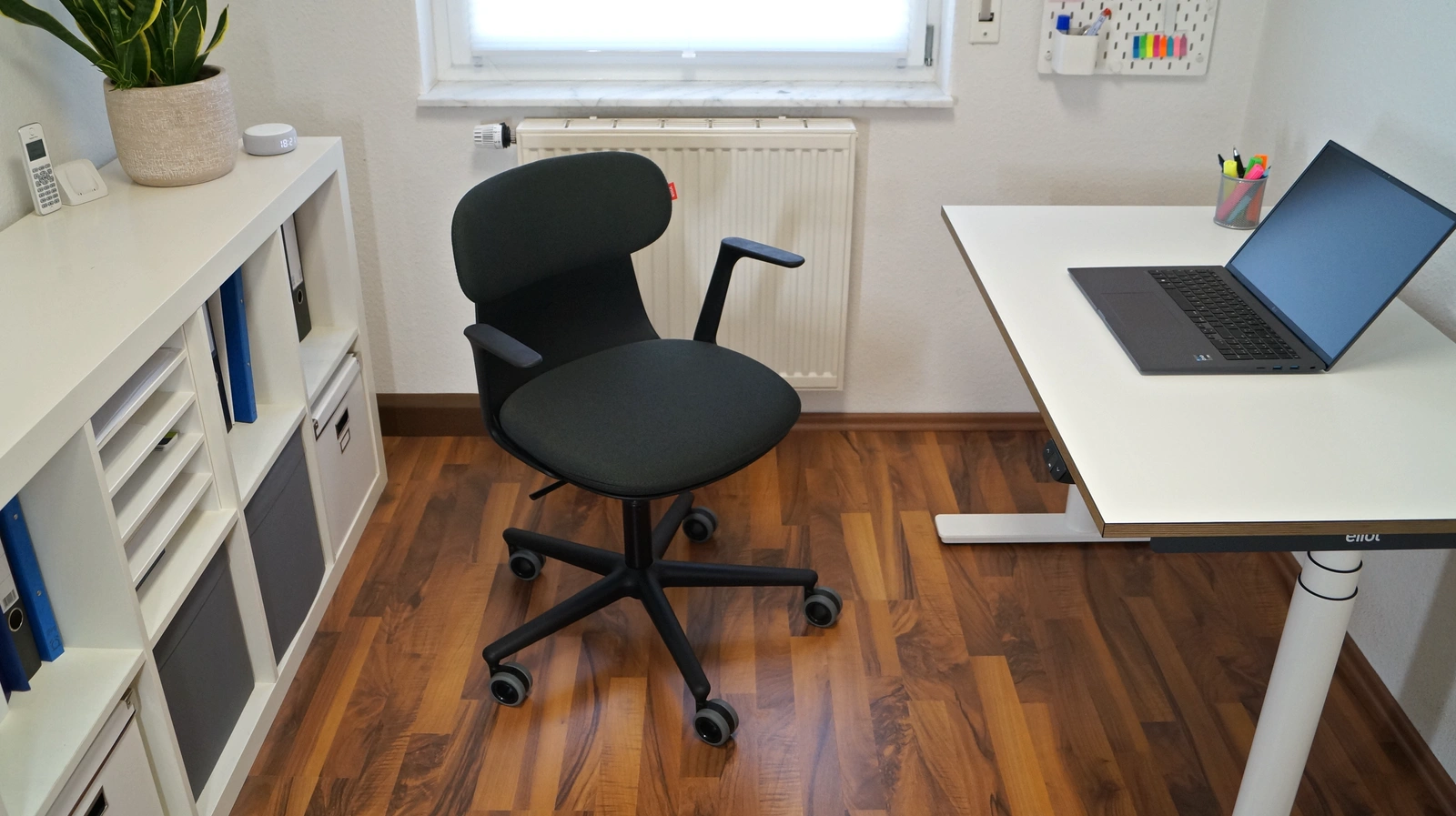 Eliot Kozy Black steht mittig im Homeoffice, links ein Regal, rechts ein Schreibtisch